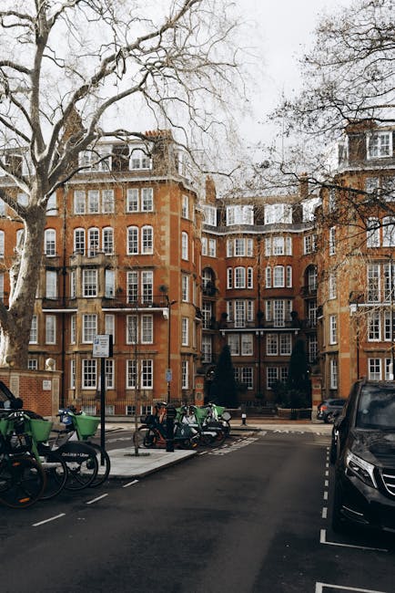 A residential building on the Portman Estate with multiple floors featuring large sash windows and brick facade, surrounded by leafless trees and parked bicycles and motorcycles on the street. In fron